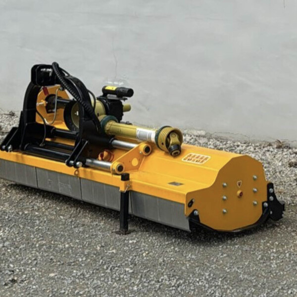Yellow hydraulic construction attachment on a tracked machine sits on gravel beside a concrete wall, ready for use.
