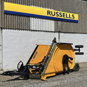 Yellow industrial wood chipper parked beside a corrugated metal wall with a blue-and-yellow Russell's sign above it.