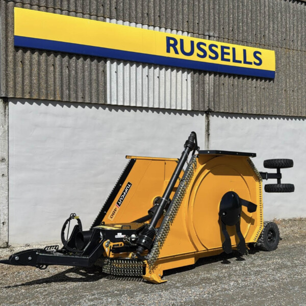 Yellow industrial wood chipper parked beside a corrugated metal wall with a blue-and-yellow Russell's sign above it.