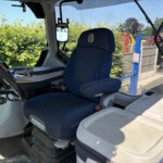 Cabin interior of a truck with a blue fabric seat labeled 'Comfort', steering wheel, and dashboard; yard equipment visible through the windows.