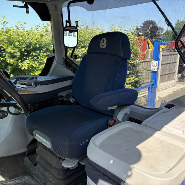 Cabin interior of a truck with a blue fabric seat labeled 'Comfort', steering wheel, and dashboard; yard equipment visible through the windows.
