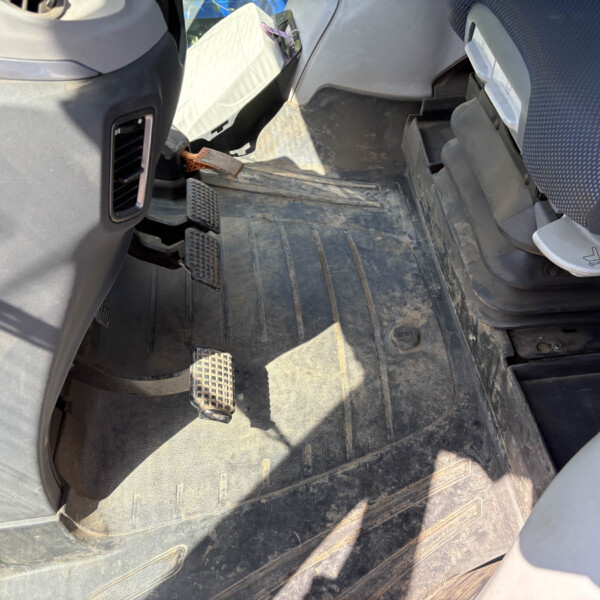 Dusty vehicle cabin floor with two pedals (brake and accelerator) and worn rubber mats nearby the driver’s seat.