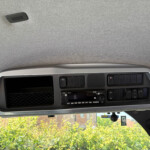 Interior of a vehicle cab ceiling with a small overhead vent and dashboard controls visible below.