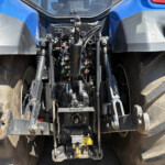 View of the tractor's rear hitch area with hydraulic levers, hoses, and large rugged tires.