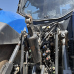 Close-up of a blue tractor front with exposed hydraulic hoses, levers, and controls.