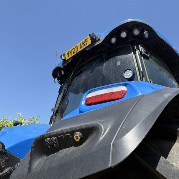 Close-up of a blue tractor front cab with a yellow license plate YY23 ANF and multiple lights against a clear blue sky.