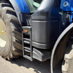 Close-up of a large tractor wheel and blue tractor body with a metal access ladder on the side