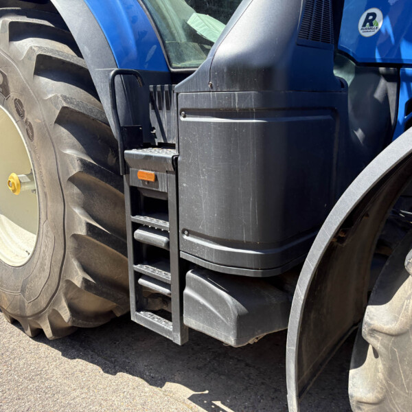 Close-up of a large tractor wheel and blue tractor body with a metal access ladder on the side