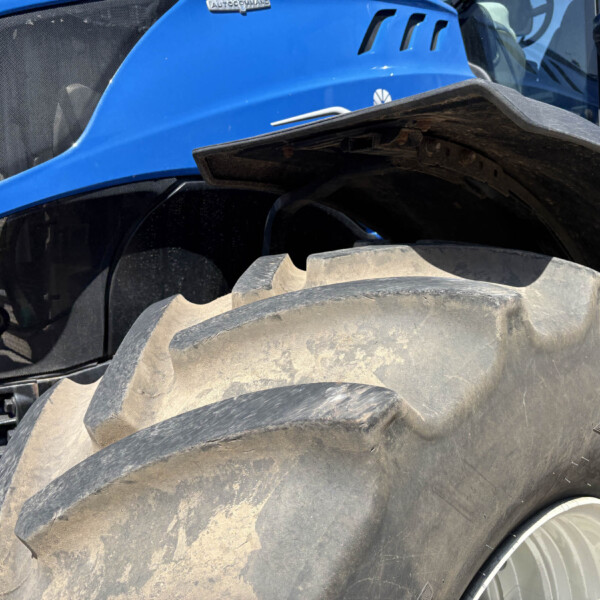 Close-up of a blue tractor body with oversized muddy tires and a black fender edge visible at the right.