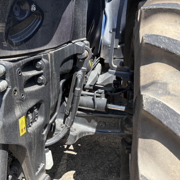 Close-up of a heavy machine’s hydraulic and chassis components beside a large treaded tire, with warning labels visible.