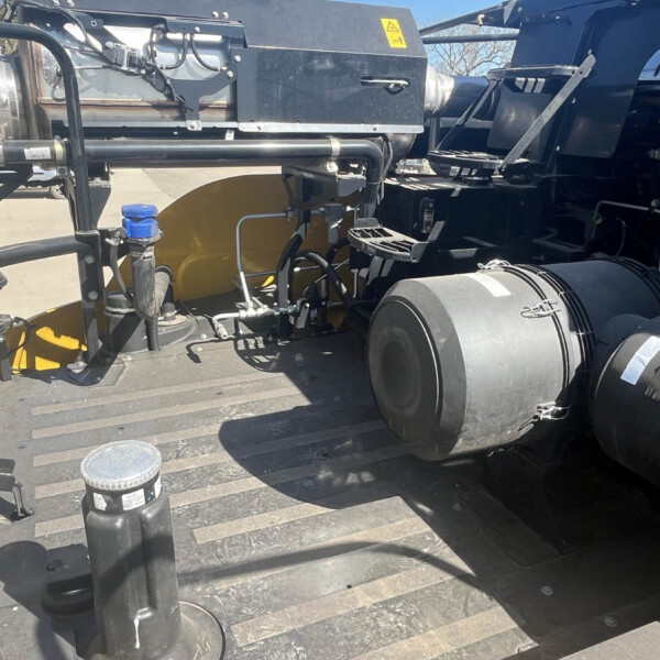 Industrial machinery mounted on a flatbed truck with hoses, ducts, and exposed wiring visible near large tires.