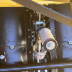 Close-up of internal mechanical components inside a dark metal housing: bolts, a spring, and a ribbed hose in an industrial machine.