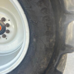 Close-up of a heavy-duty tractor tire with a white rim and rusted lug nuts, showing deep treads and dirt.