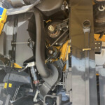 Close-up of heavy industrial machinery interior with gears, belts and yellow safety panels in view.