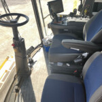 Interior of a tractor cab with a steering wheel on the left and a control console with buttons and a screen in the center.