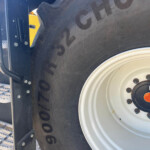 Close-up of a large tractor tire with a white rim, blue chassis, and a yellow component nearby.