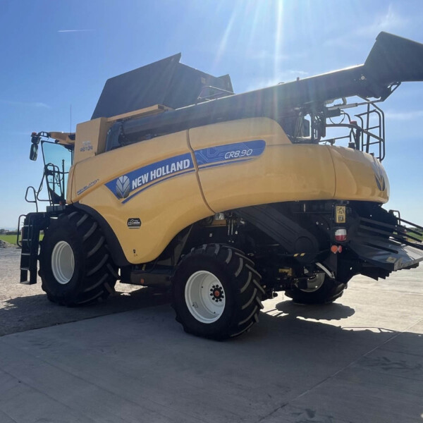 New Holland CR8.90 combine harvester parked on a concrete lot under a bright blue sky with the header raised.