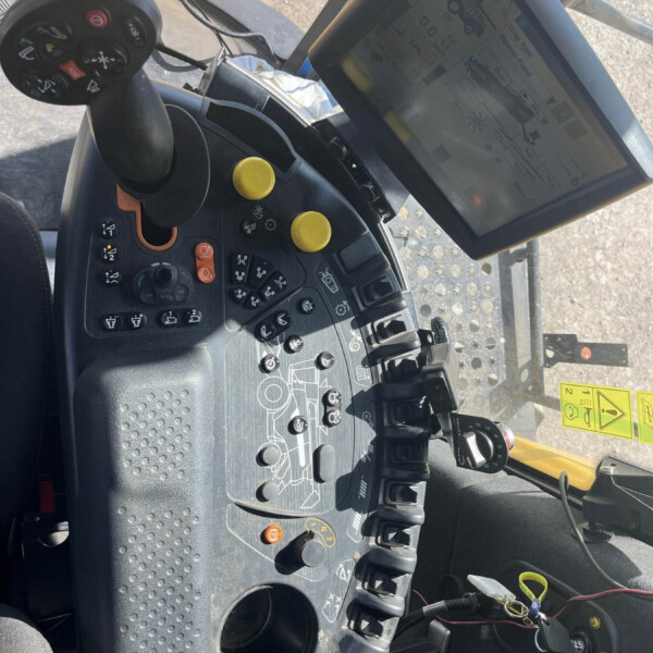 Cockpit of a tractor showing a joystick, yellow control knobs, and a large mounted display screen with gauges and controls nearby.