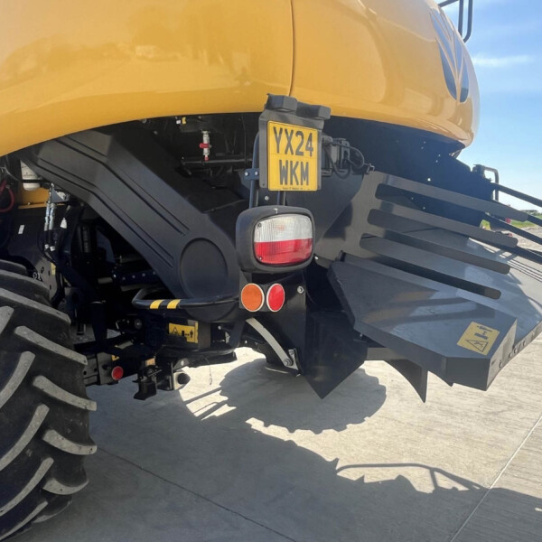 Rear view of a yellow agricultural machine with large tires, showing the license plate YX24 WKM and rear lights on a concrete surface.