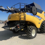 Yellow New Holland CR8.90 combine harvester with header attached, parked on a concrete lot under a blue sky