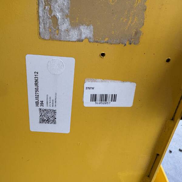 Yellow metal surface with two white labels, a visible QR code, and a barcode; some peeling paint and a small hole indicate wear.