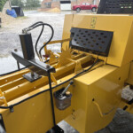 Yellow industrial machine with hydraulic hoses, control panels, and metal frames in an outdoor yard.