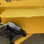 Close-up of a yellow industrial machine with a black metal attachment and tangled white cables resting on a yellow surface.