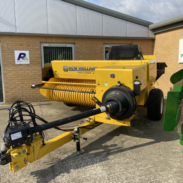 Yellow New Holland hay baler outside a brick building with a Russell Group sign visible nearby.