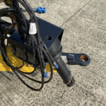 Close-up of tangled black hoses and cables attached to a yellow piece of machinery on a concrete surface, with blue tape and white tags visible.