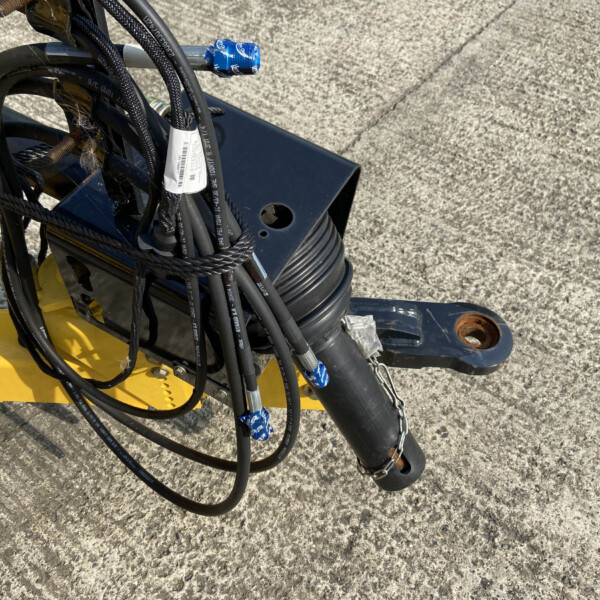 Close-up of tangled black hoses and cables attached to a yellow piece of machinery on a concrete surface, with blue tape and white tags visible.