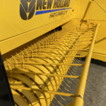 Close-up of a bright yellow New Holland hay baler header with curved tines and the 'Hayliner 275' branding visible on the side.