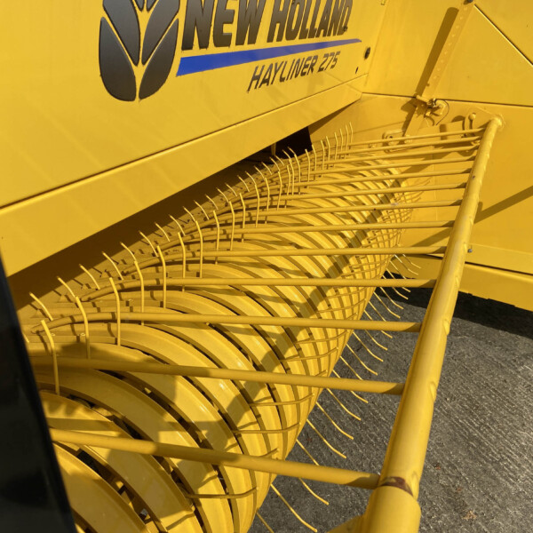 Close-up of a bright yellow New Holland hay baler header with curved tines and the 'Hayliner 275' branding visible on the side.