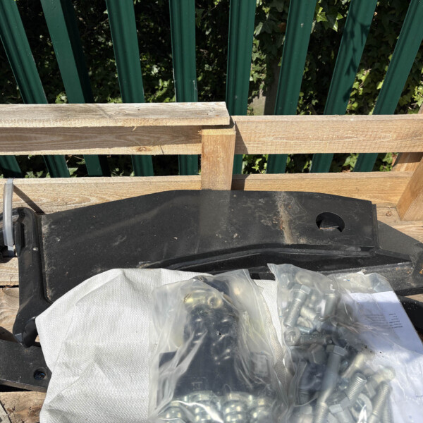 Top-down view of a weathered wooden pallet with a black plastic container and a clear bag of metal hardware, set against a green vertical fence background.