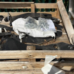 Hardware pieces and fasteners scattered on a wooden pallet, including bolts in a plastic bag and metal brackets.