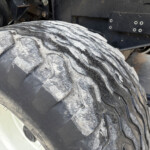 Close-up of a large, dusty tractor tire with deep treads, white wheel rim, and dark metal chassis in the background.