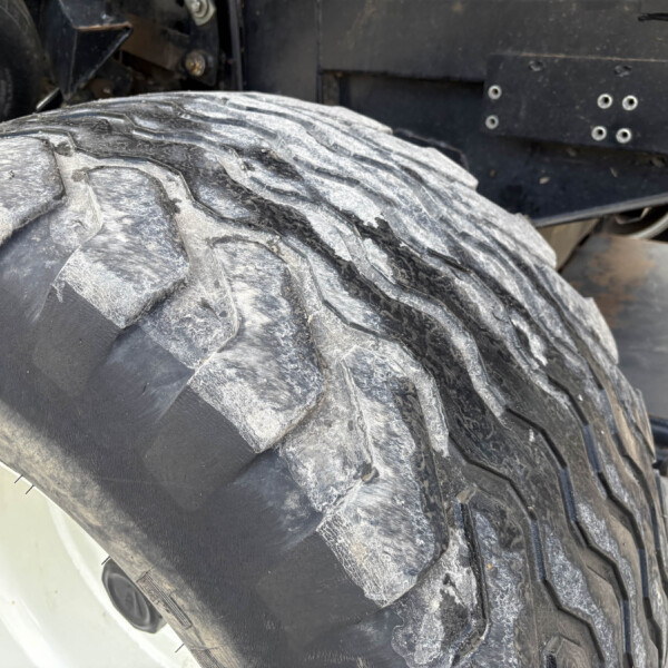 Close-up of a large, dusty tractor tire with deep treads, white wheel rim, and dark metal chassis in the background.
