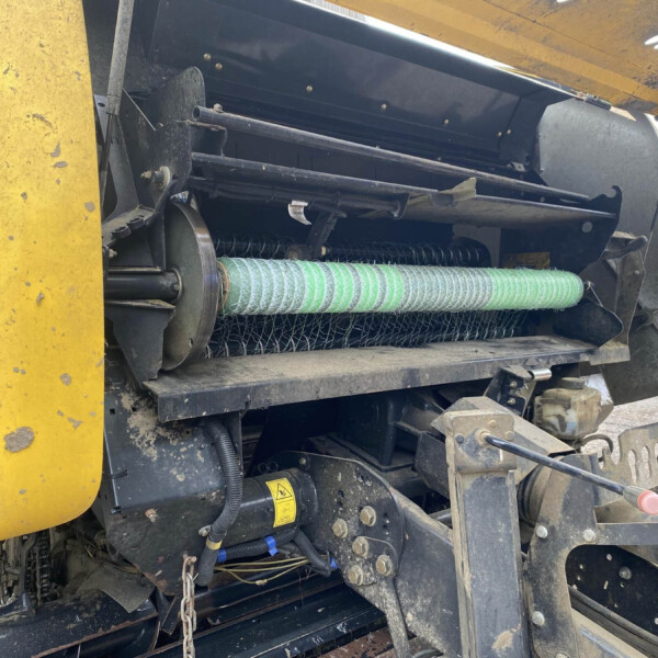 Close-up of green spiral belt and metal rollers inside a yellow agricultural machine, showing exposed mechanical parts.