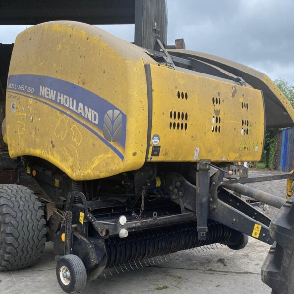 Yellow New Holland Roll-Belt 150 combine harvester on a trailer, dusty with a blue stripe along the side.