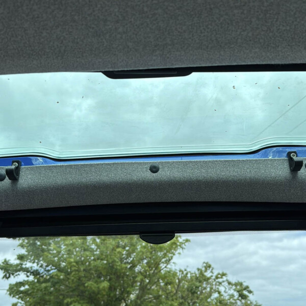 Open sunroof in a vehicle showing blue sky and treetops outside, with gray fabric headliner and interior trim around the glass opening