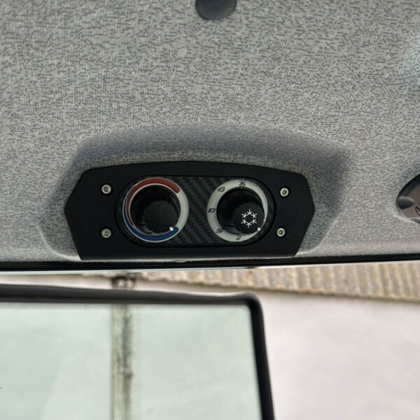 Overhead vehicle ceiling with climate control panel featuring two circular dials and two dome lights on a gray fabric headliner.