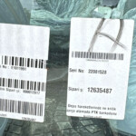 Two white barcode labels with serial numbers and Turkish text stuck to a plastic-wrapped package inside a car window.