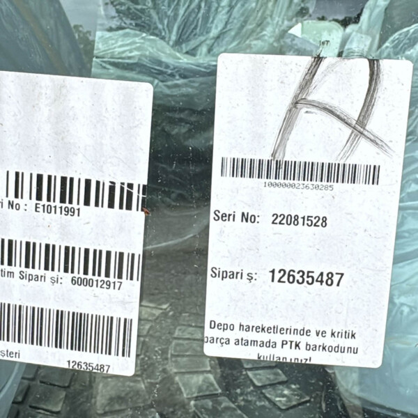 Two white barcode labels with serial numbers and Turkish text stuck to a plastic-wrapped package inside a car window.