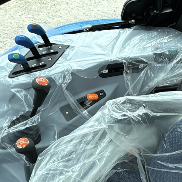 Cockpit with multiple blue-handled levers and an orange knob, all covered in protective plastic wrap inside a vehicle cab.
