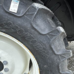 Close-up of a tractor rear tire with large tread, gray rim, and blue fender on gravel.