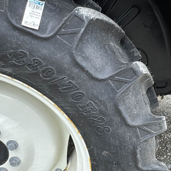 Close-up of a tractor rear tire with large tread, gray rim, and blue fender on gravel.