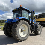 Blue modern tractor parked outdoors with oversized front tires and an orange beacon on top, near a metal building in a rural area.