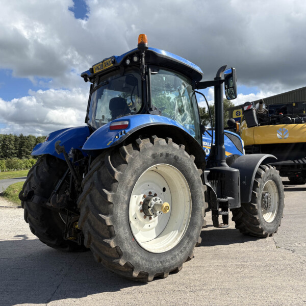 Blue modern tractor parked outdoors with oversized front tires and an orange beacon on top, near a metal building in a rural area.
