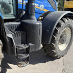 Close-up of large tractor tires and black access steps on blue heavy equipment, dusty ground nearby