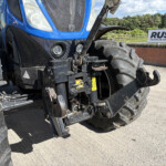 Close-up of a blue tractor front with hydraulic hitch and oversized tires, a Russell sign visible in the background.