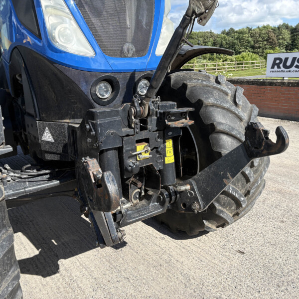 Close-up of a blue tractor front with hydraulic hitch and oversized tires, a Russell sign visible in the background.